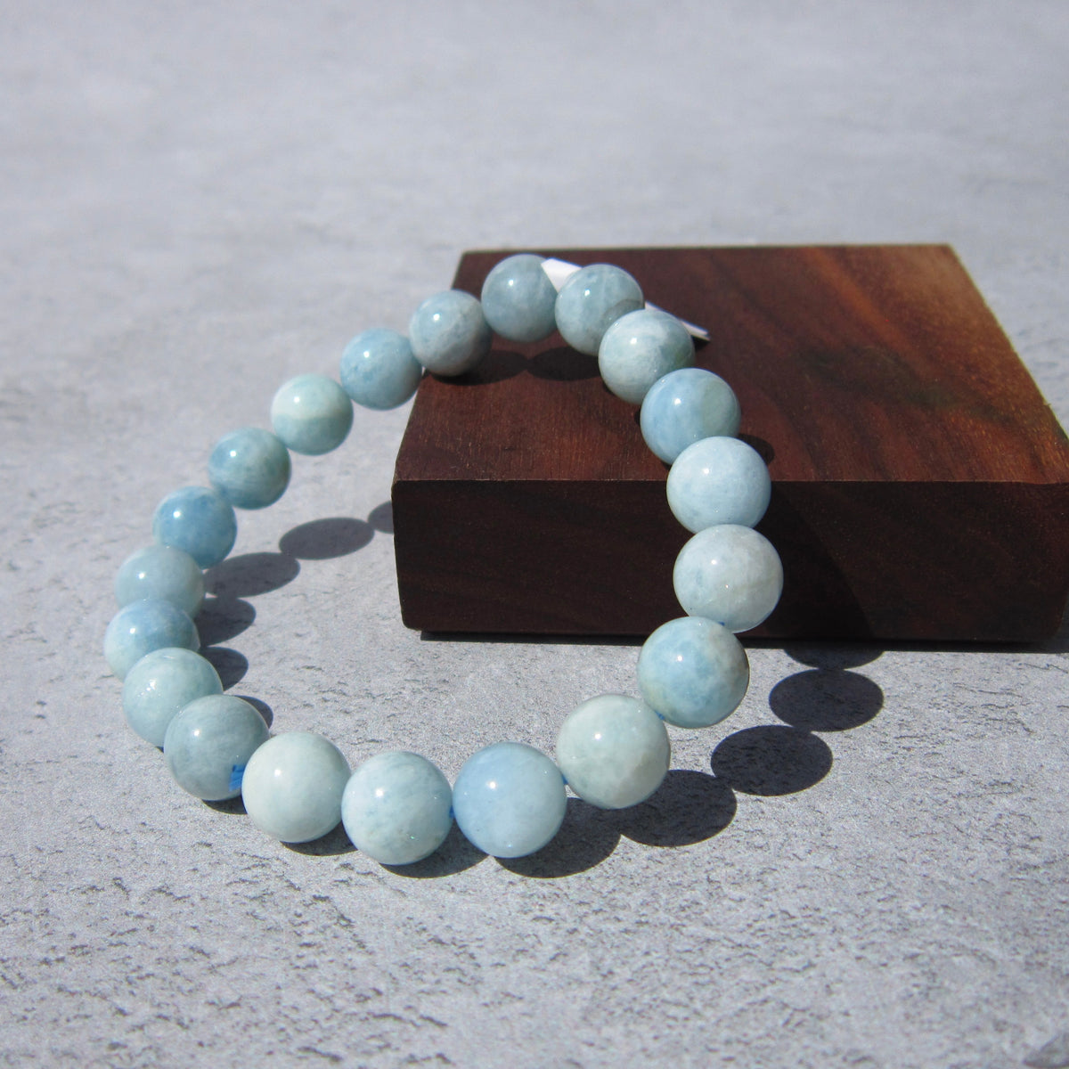 The Healing Hedge Witch Aquamarine Crystal Bracelet is shown on a gray surface beside a brown wooden block under bright light.