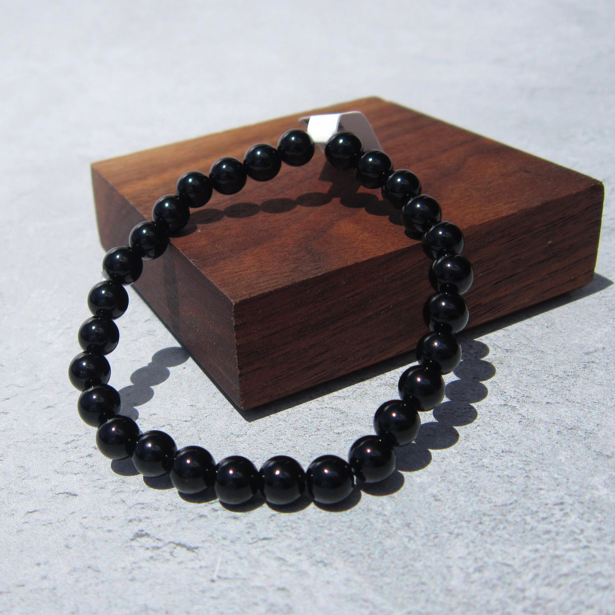 The Healing Hedge Witch's Obsidian Bracelet, known for grounding and protection, is displayed in a circle on a light gray surface, partly resting on a square wooden block.