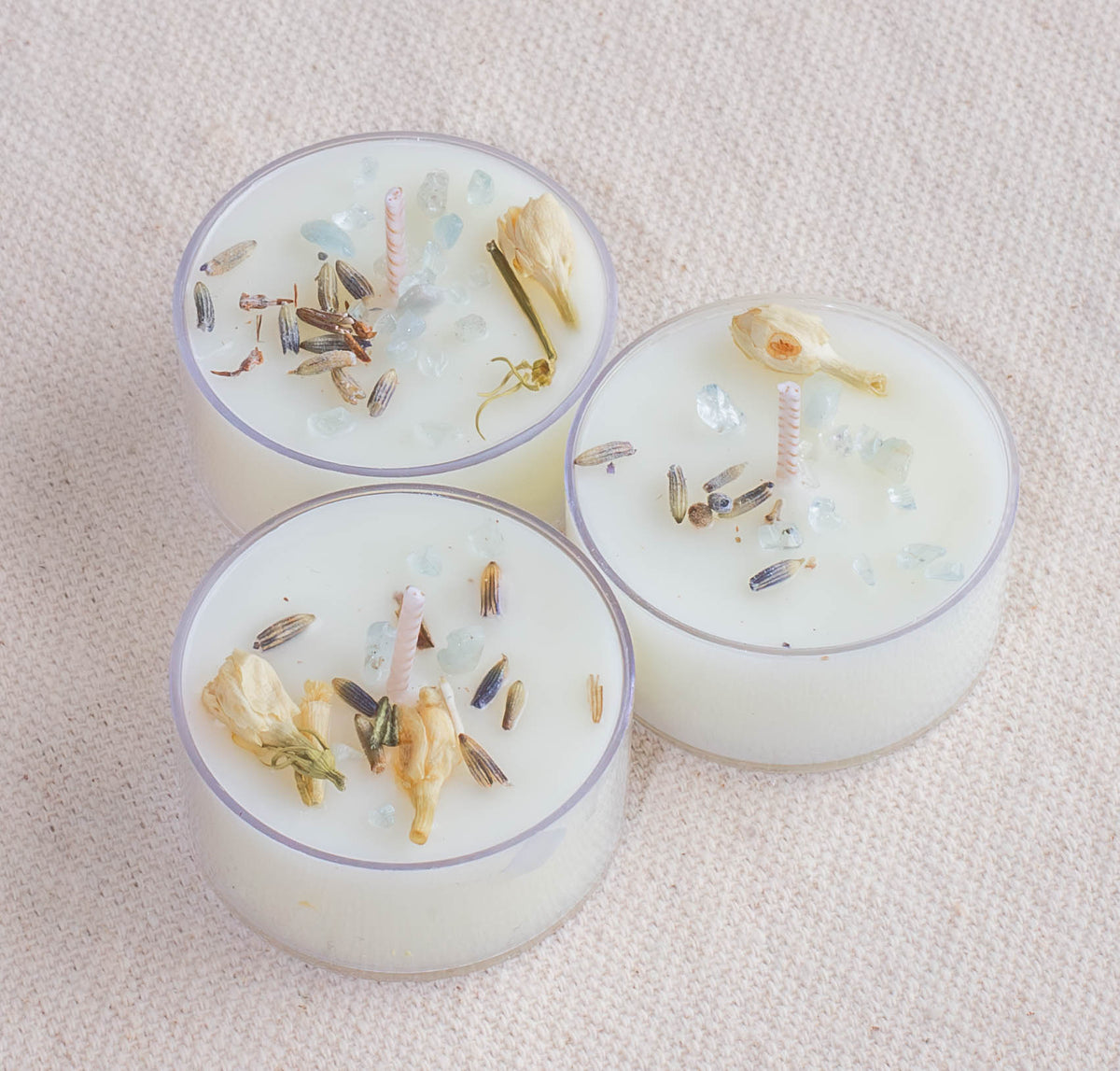 The Healing Hedge Witch Spring Equinox Spell Tealights feature three white candles in clear holders, each topped with dried flowers, lavender buds, and crystals—ideal for rituals, manifestations, or creating a calming ambiance.