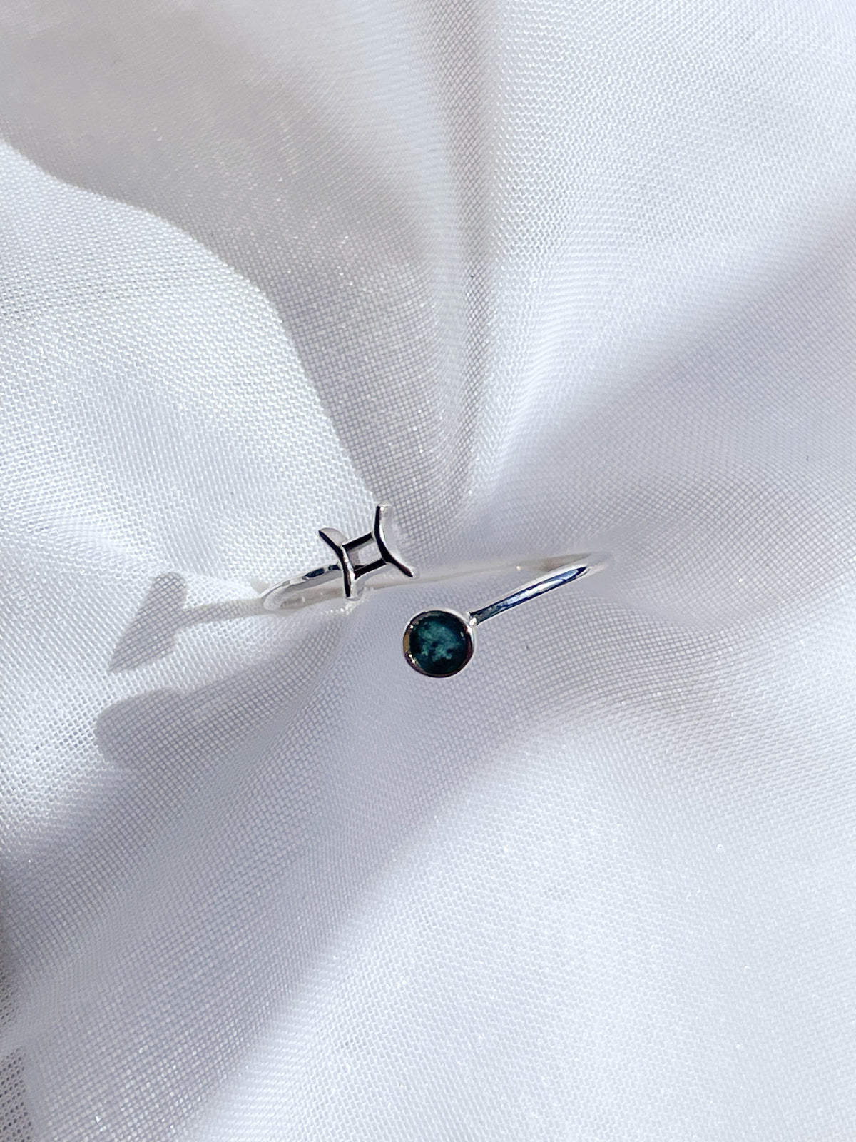 The Healing Hedge Witch Zodiac Sterling Silver Ring features the Pisces symbol and a round blue-green birthstone, shown on a white textured fabric background.