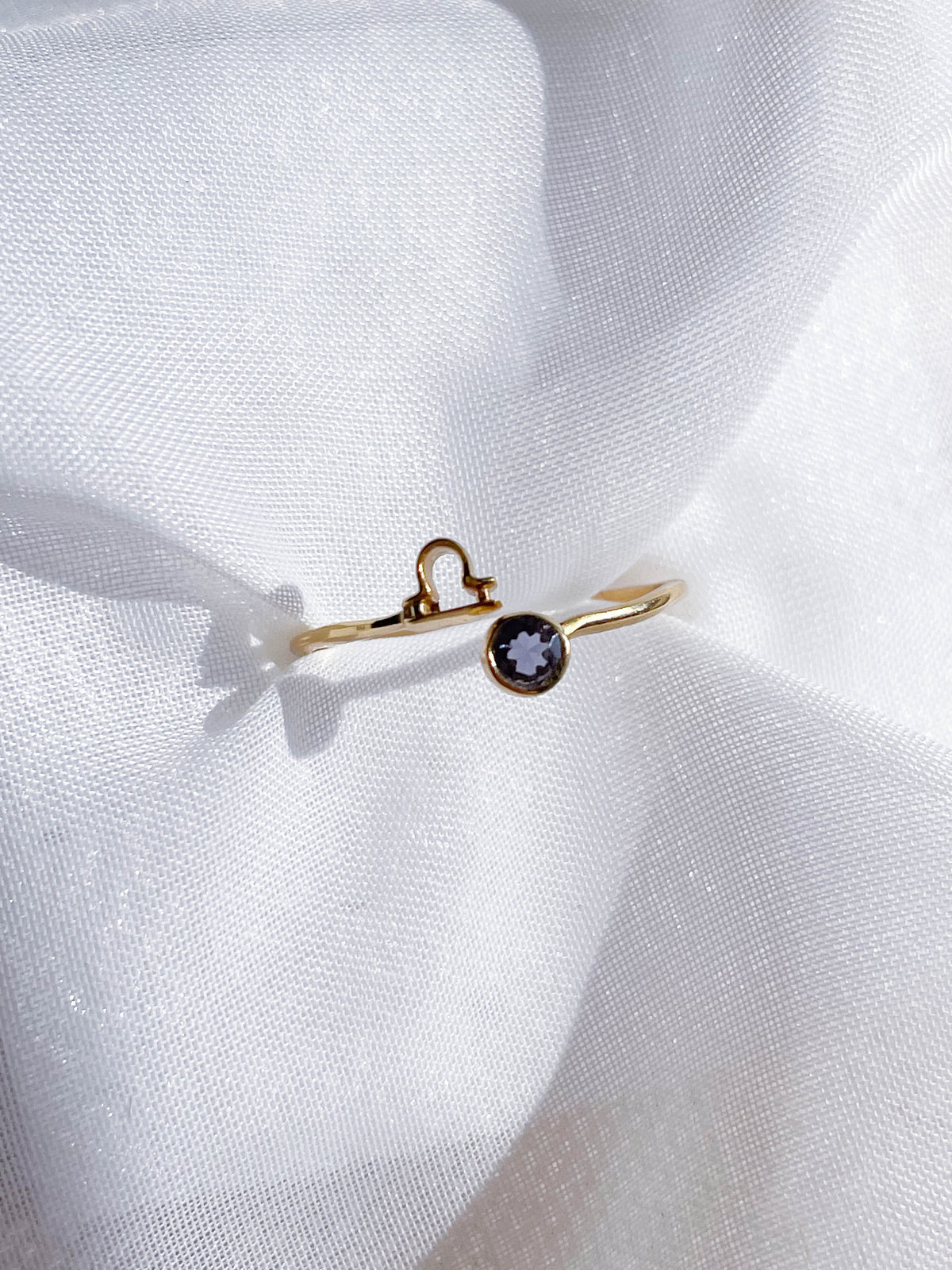 The Healing Hedge Witch Zodiac Gold Plated Ring, featuring a small round birthstone and a Libra symbol, rests on white textured fabric in soft natural light.