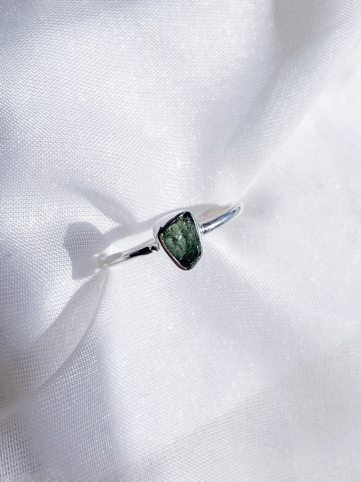 The Healing Hedge Witch Green Tourmaline Rough Sterling Silver Crystal Necklace features a unique green gemstone centerpiece, beautifully displayed on a soft white fabric background.