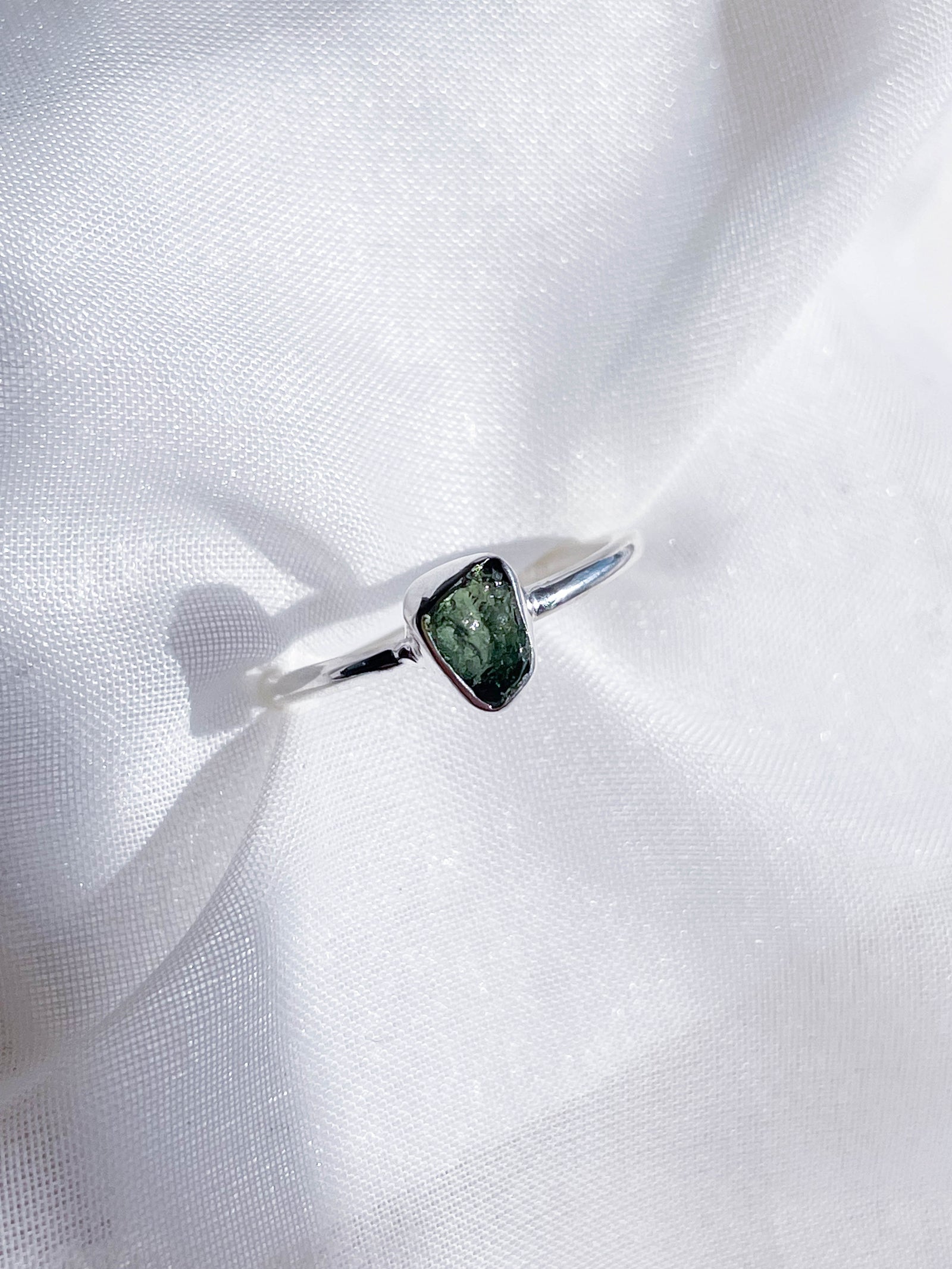 The Healing Hedge Witch Green Tourmaline Rough Sterling Silver Crystal Necklace features a unique green gemstone centerpiece, beautifully displayed on a soft white fabric background.