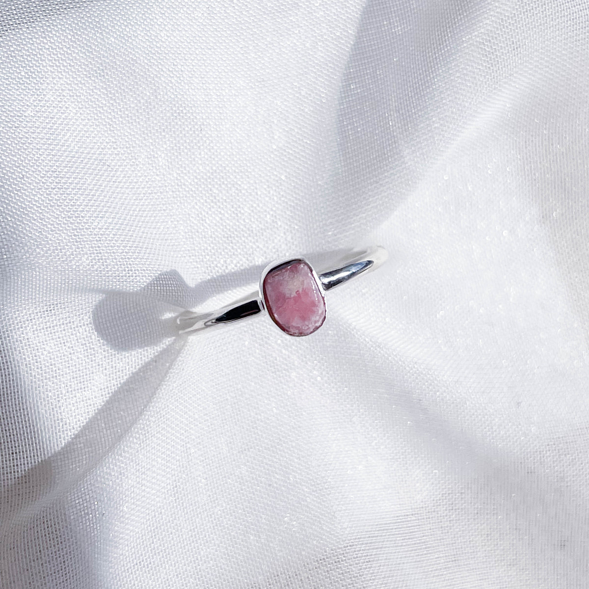 The Healing Hedge Witch's Rhodochrosite Rough Sterling Silver Crystal Necklace is displayed on softly textured white fabric, highlighted by natural light.