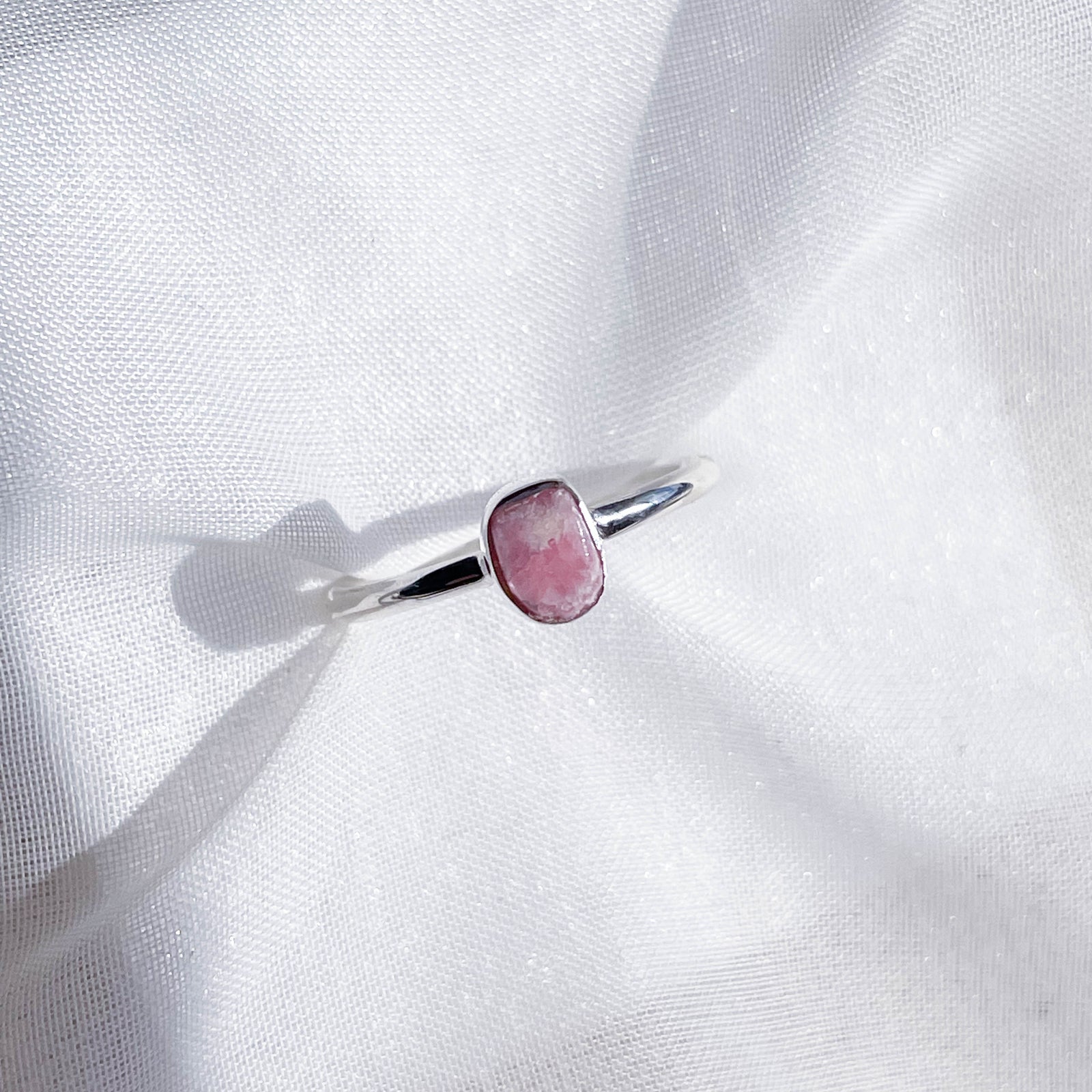 The Healing Hedge Witch's Rhodochrosite Rough Sterling Silver Crystal Necklace is displayed on softly textured white fabric, highlighted by natural light.