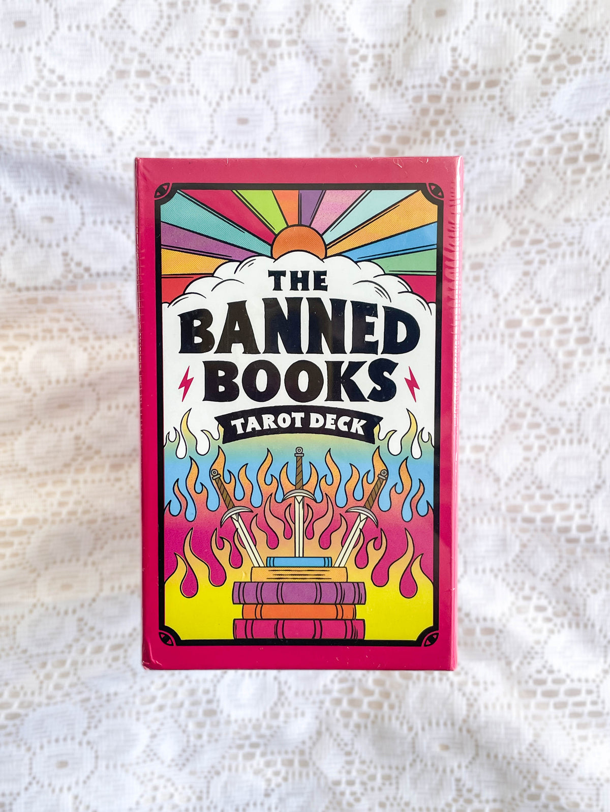 A pink box featuring a colorful design, containing the Banned Books Tarot by The Healing Hedge Witch.