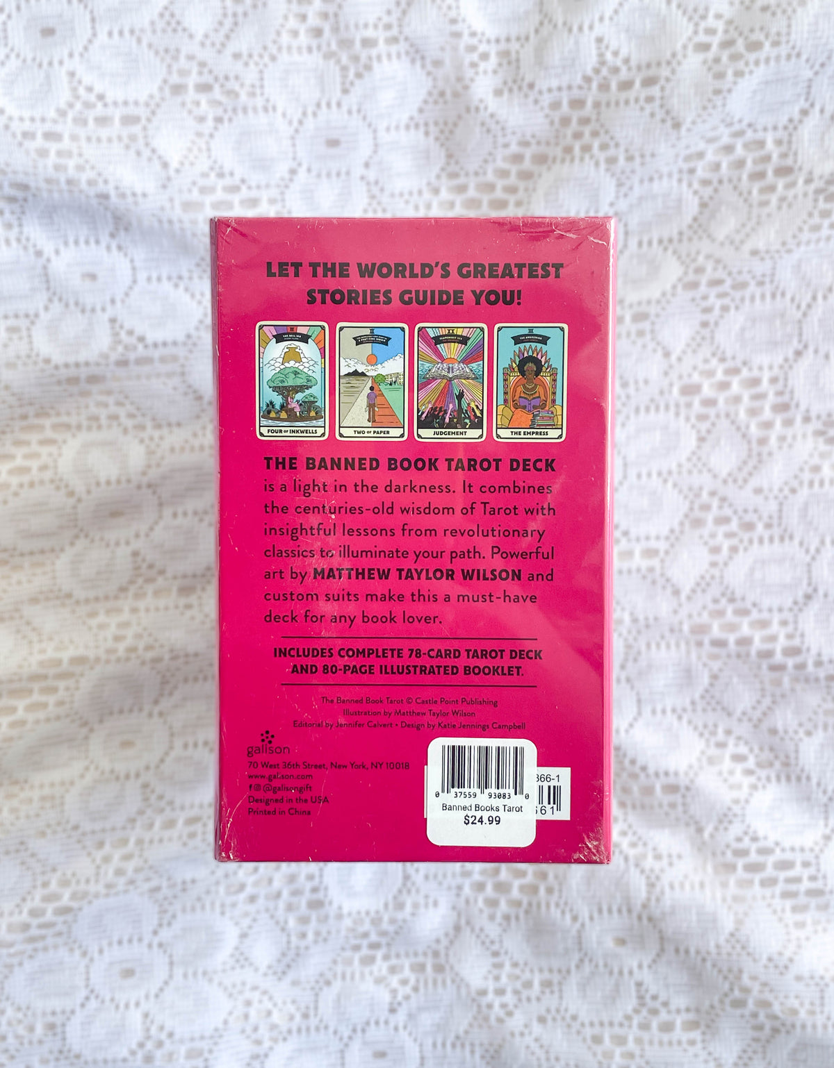 The back of a pink Banned Books Tarot box by The Healing Hedge Witch rests on lace, displaying images of four tarot cards, descriptive text about the deck, a barcode, and a price sticker.