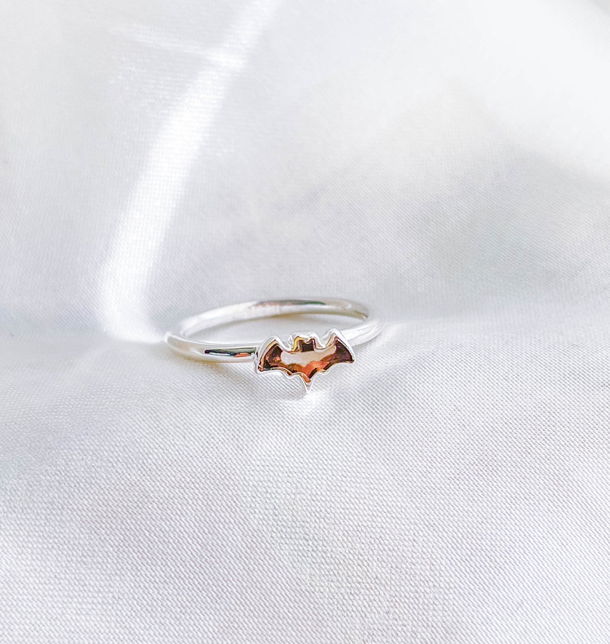 The Healing Hedge Witch Smoky Quartz Bat Crystal Stackable Ring features a small bat design atop a silver band, shown on smooth white fabric.