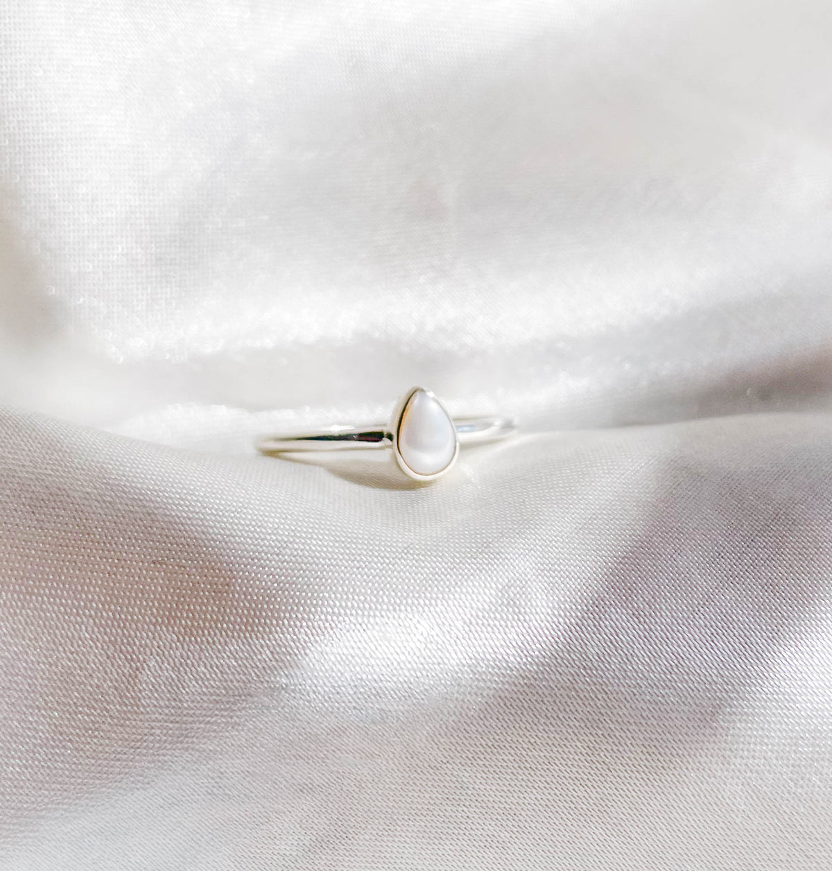 The Healing Hedge Witch’s Pearl Stackable Ring features a delicate silver band with a teardrop-shaped white pearl, shown on soft white satin.