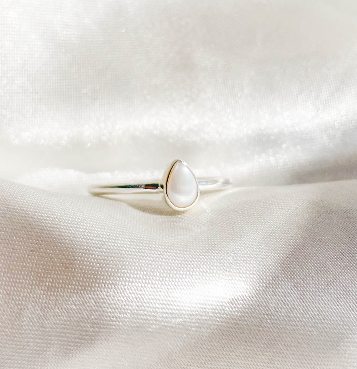 The Healing Hedge Witch Pearl Stackable Ring features a teardrop-shaped white pearl set in silver, shown on white satin fabric.