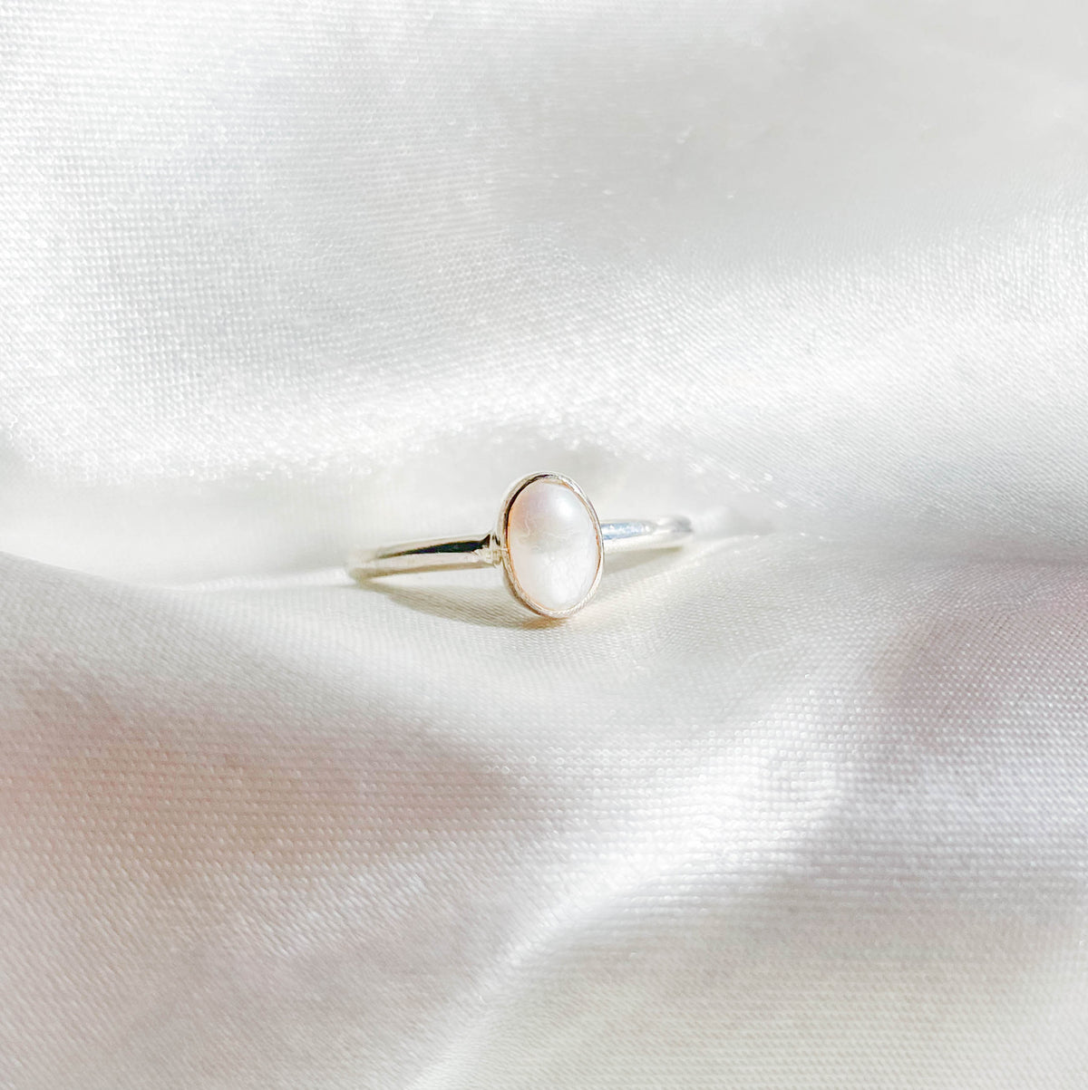 The Healing Hedge Witch Mother of Pearl Stackable Ring features a delicate silver band with an oval mother of pearl gemstone, elegantly displayed on soft white satin.
