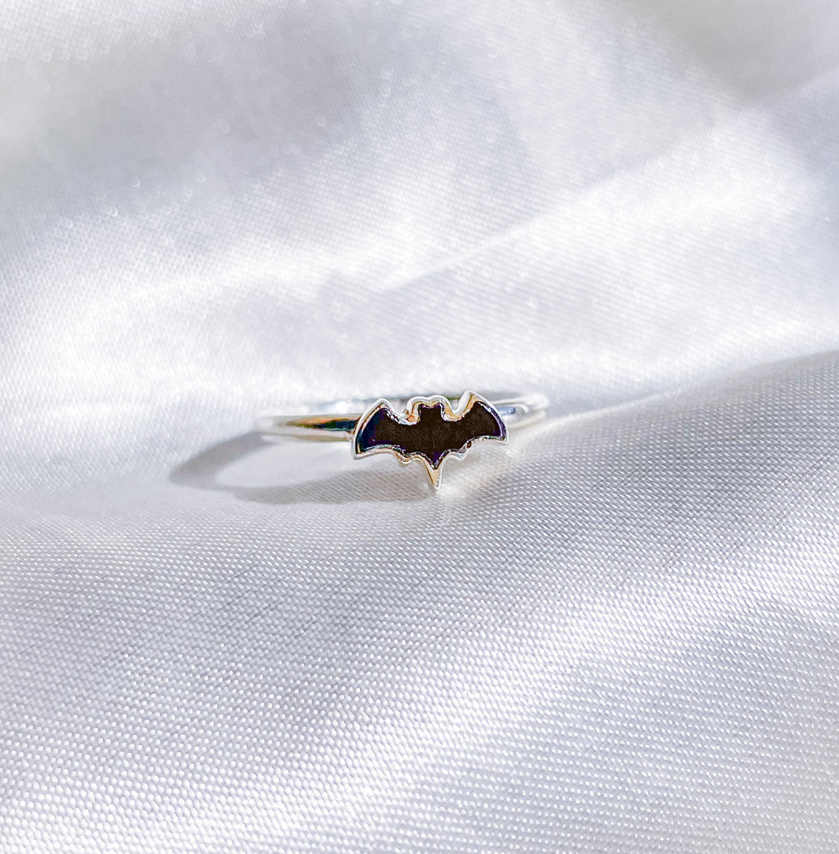 The Healing Hedge Witch Black Tourmaline Bat Crystal Stackable Ring is shown on a white, silky fabric background.