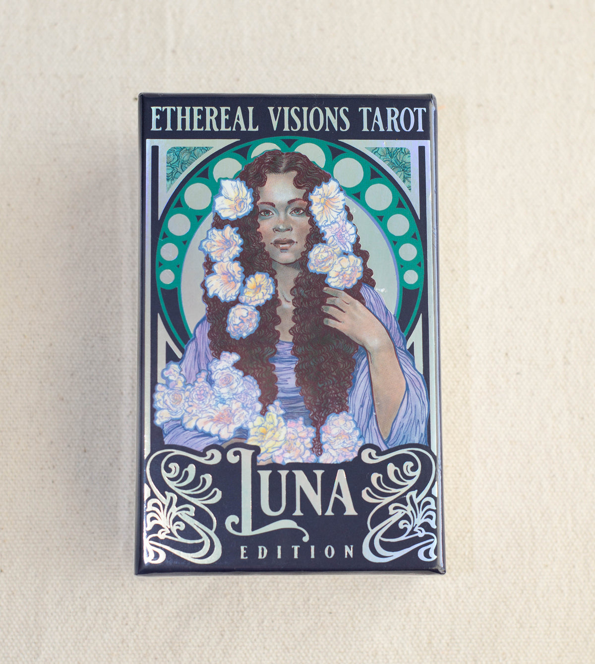 A box of Ethereal Visions Tarot Luna Edition by The Healing Hedge Witch, an Art Nouveau tarot featuring a woman with long brown hair, white flowers, and decorative green and silver designs.
