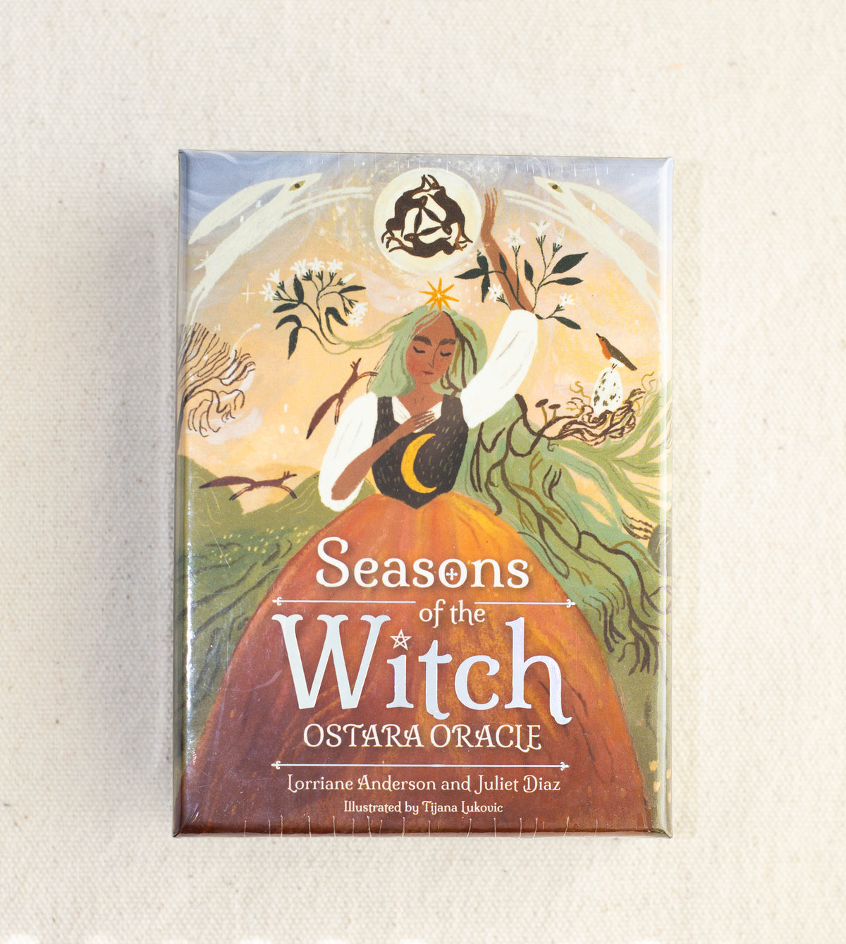 The Healing Hedge Witch's Seasons of the Witch Ostara Oracle box features an illustrated woman in a green and orange dress with long hair, surrounded by branches, leaves, and mystical symbols.