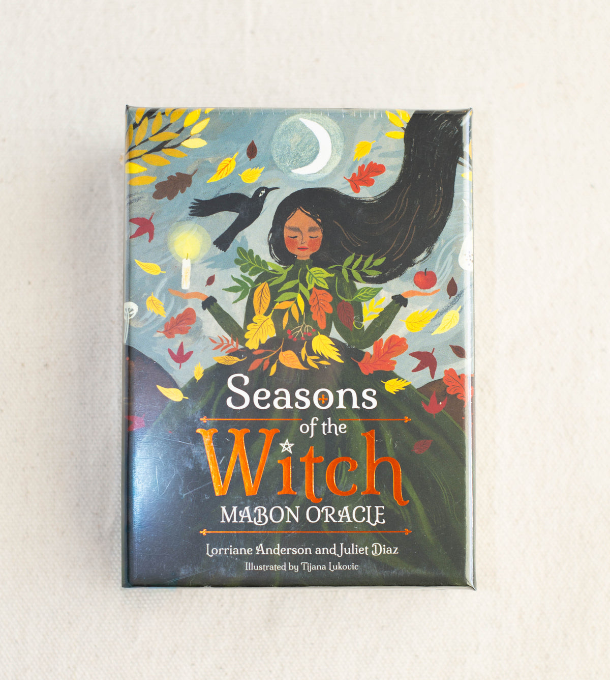 The Healing Hedge Witch’s Seasons of the Witch Mabon Oracle deck box shows an illustrated woman with long hair, autumn leaves, a raven, a crescent moon, and swirling wind set against a dark background.
