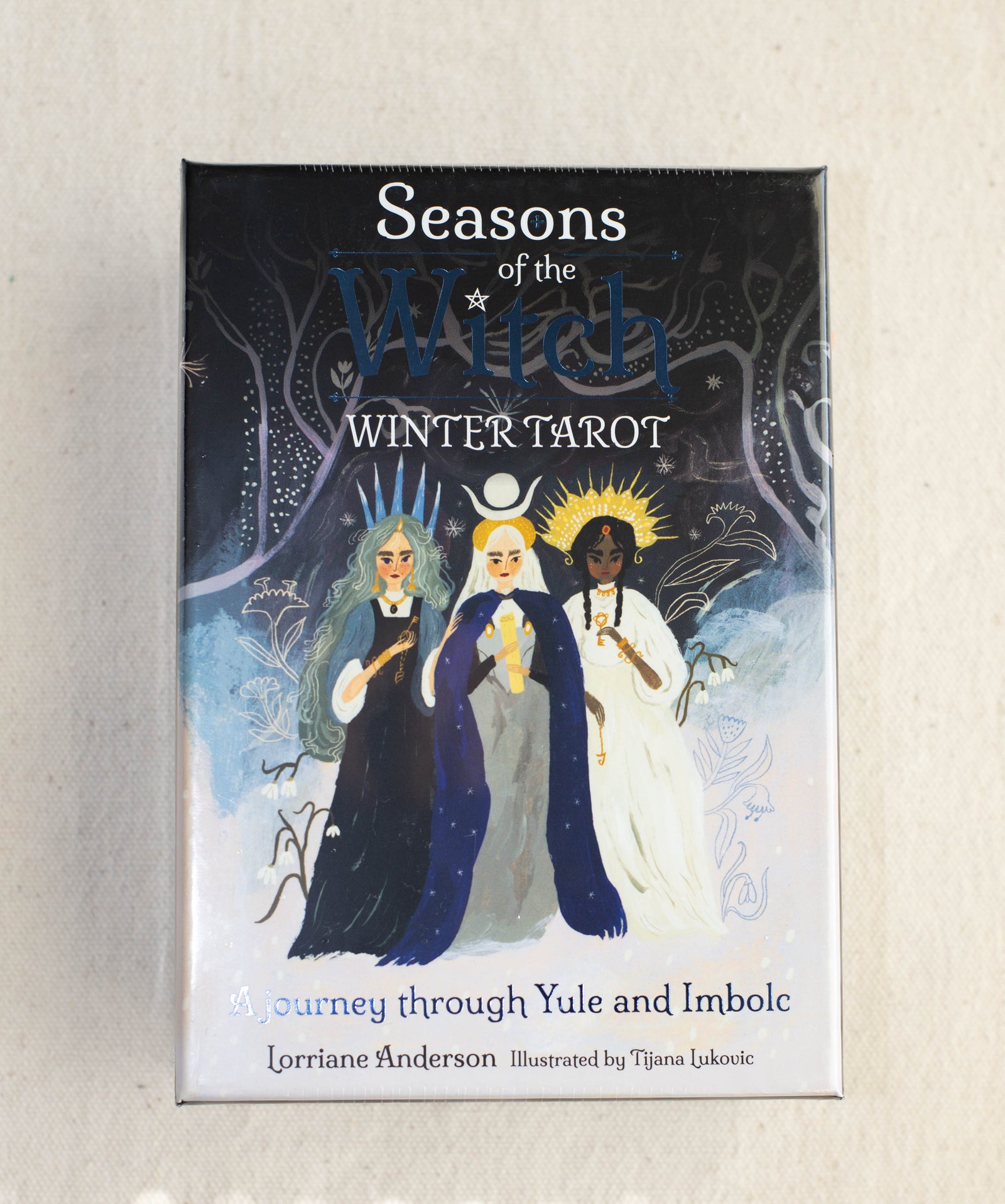Box cover of The Healing Hedge Witch’s Seasons of the Witch Winter Tarot, featuring three women in dark, blue, and white robes under moonlight, holding candles amid winter trees.
