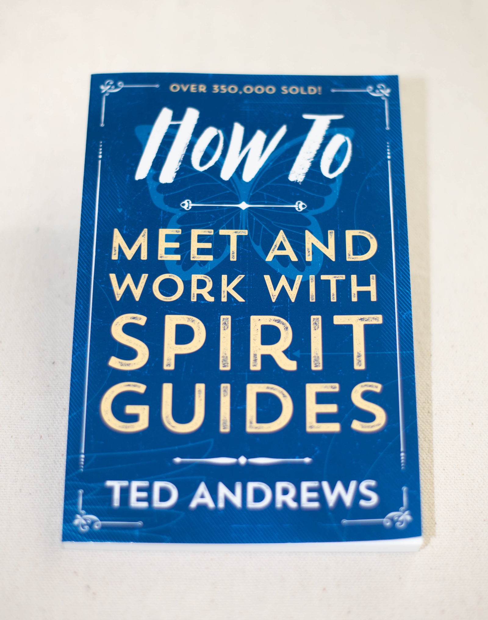 A blue book titled "How To Meet And Work With Spirit Guides" by The Healing Hedge Witch lies on a light surface, with "Over 350,000 sold!" in white text at the top of the cover.