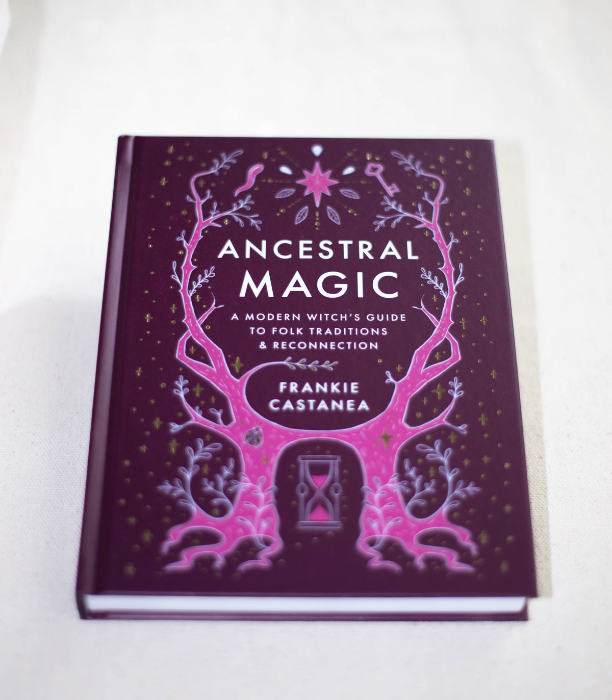 A purple book titled Ancestral Magic by The Healing Hedge Witch features mystical pink tree branches, stars, and an hourglass on the cover.