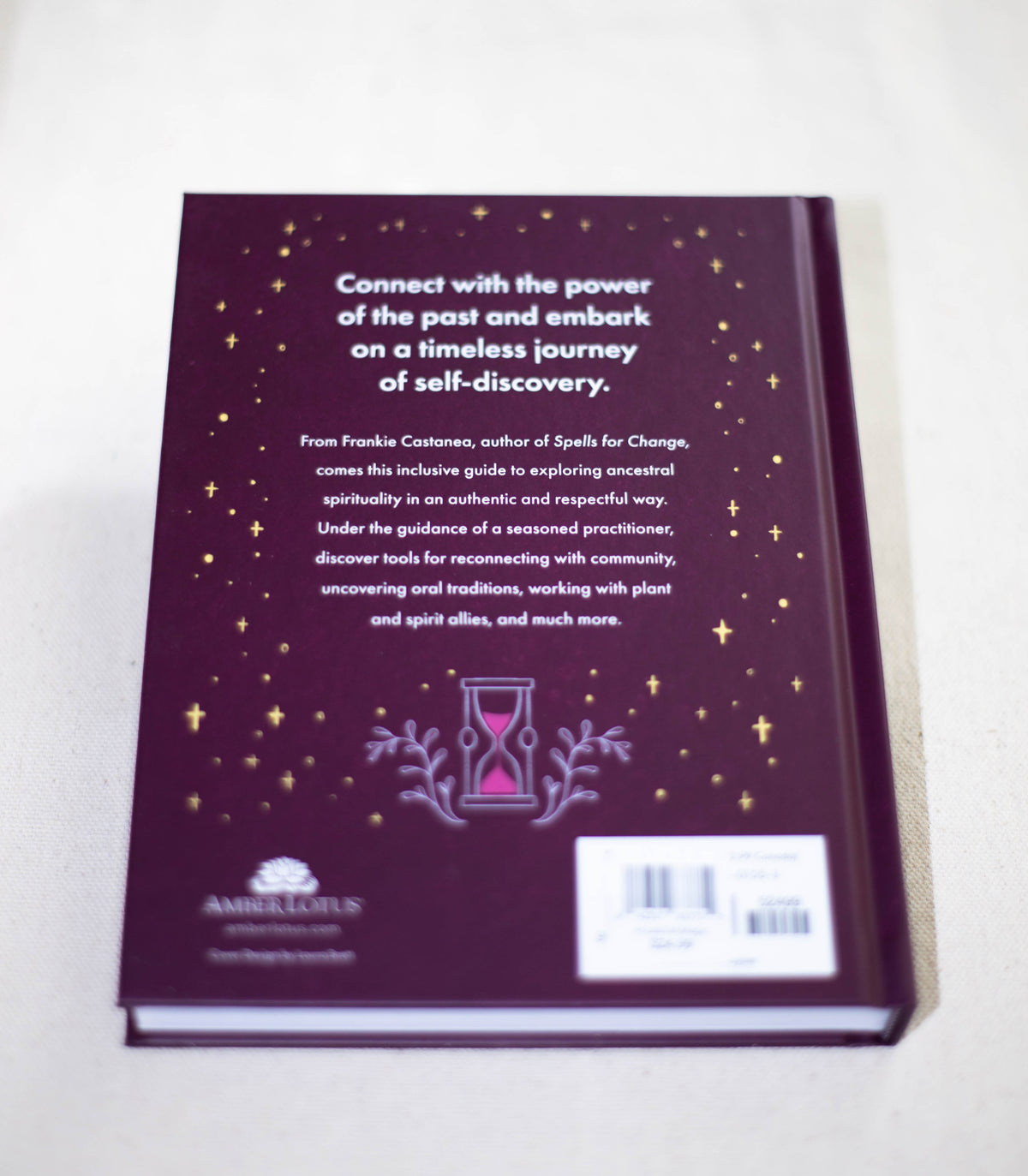 The back cover of "Ancestral Magic" by The Healing Hedge Witch features a description of ancestral spirituality and self-discovery, adorned with small gold stars, an hourglass illustration, and publisher details at the bottom.