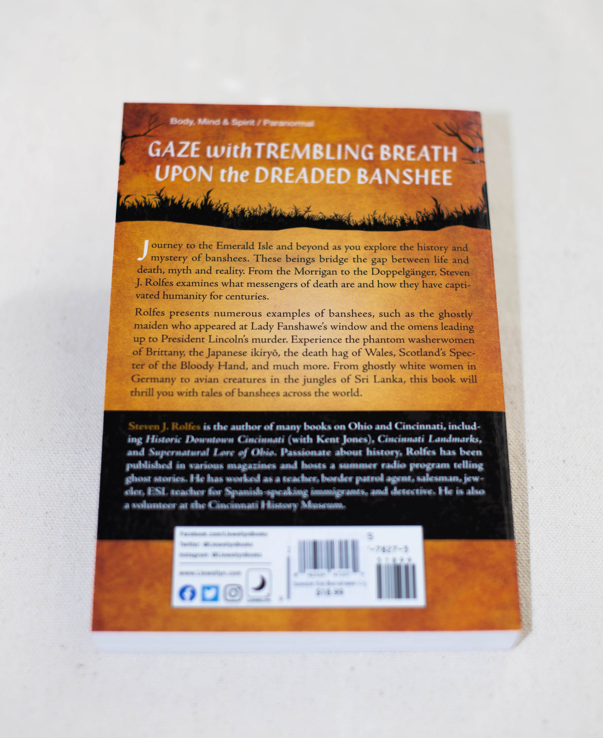 The back cover of Beware the Banshees Cry by The Healing Hedge Witch shows a summary of banshee history, a barcode, and publisher details at the bottom. The in-focus image is set on a white background.