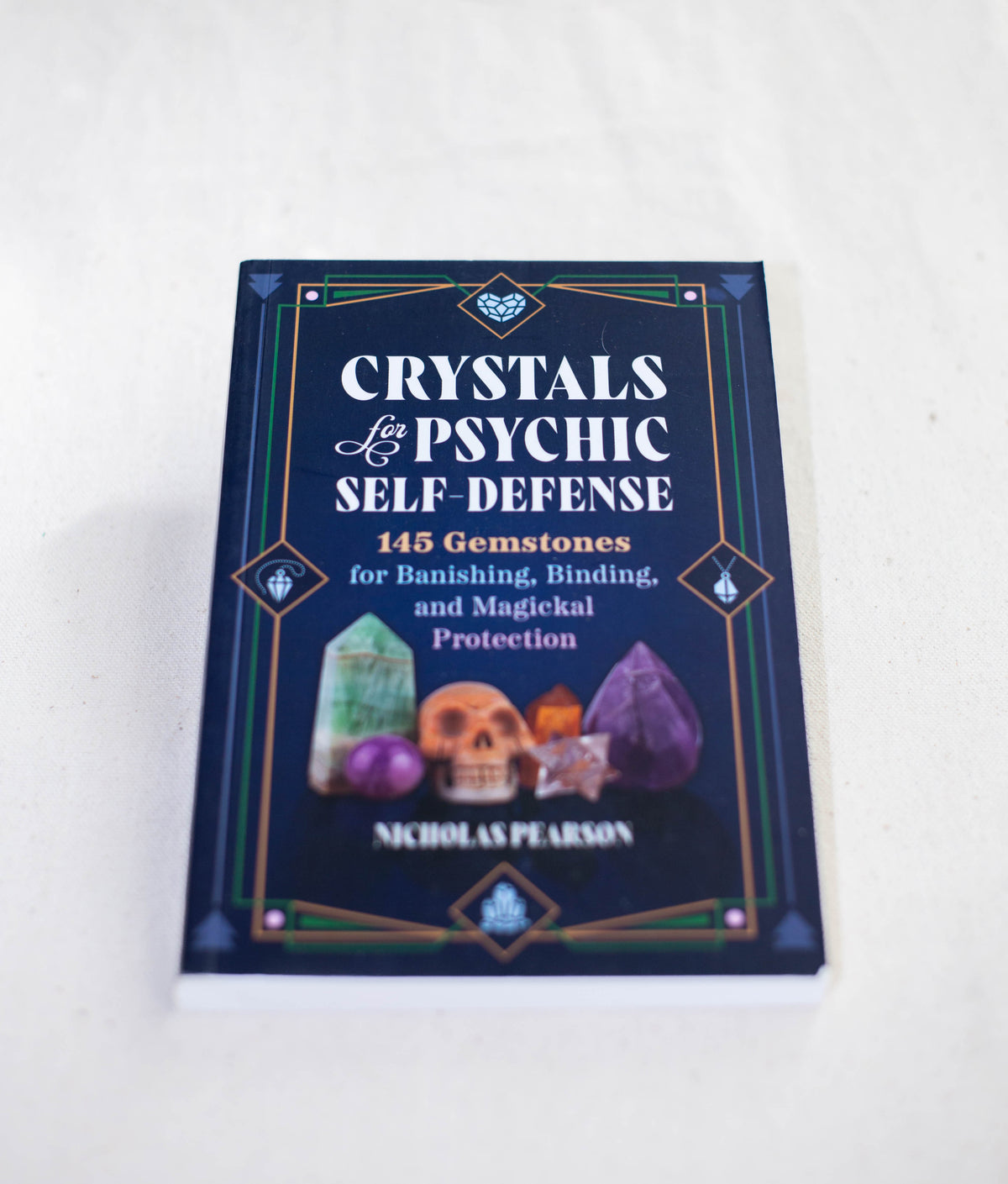 Crystals For Psychic Self-Defense by The Healing Hedge Witch rests on a white surface, its cover adorned with gemstone illustrations and mystical symbols.