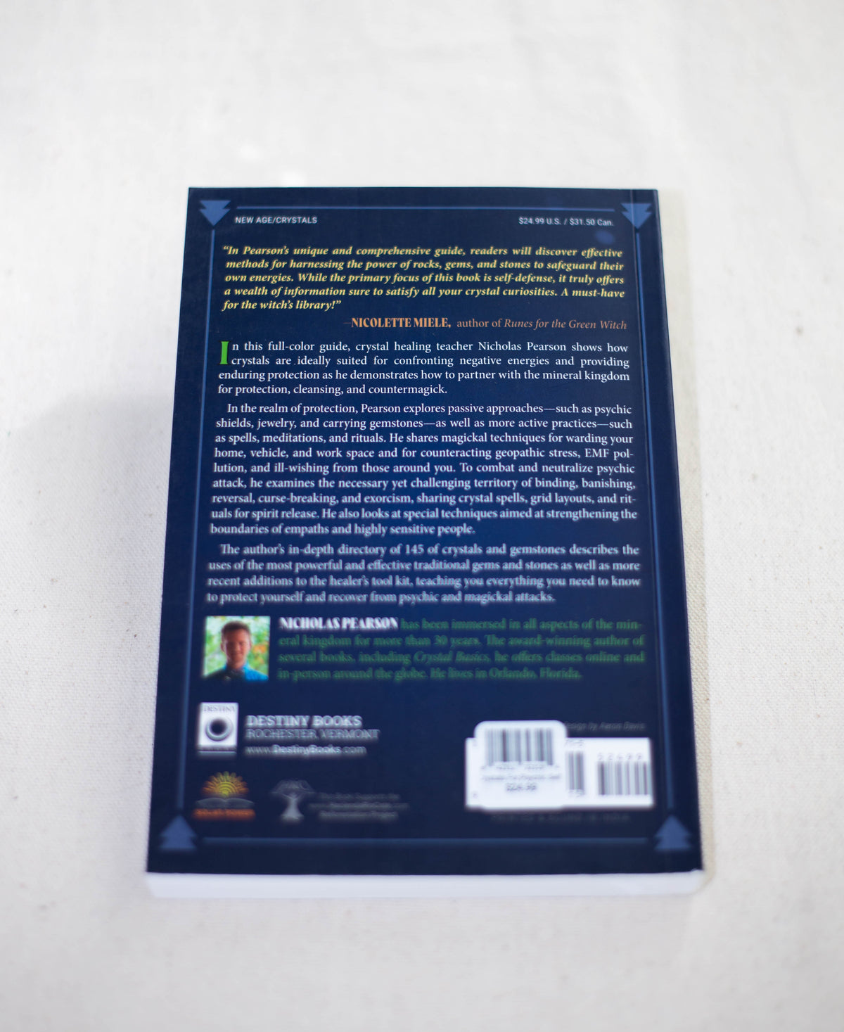 The back cover of Crystals For Psychic Self-Defense by The Healing Hedge Witch includes a synopsis, endorsements, a small author photo, publisher logos, and a barcode. The background is dark blue with yellow and white text.