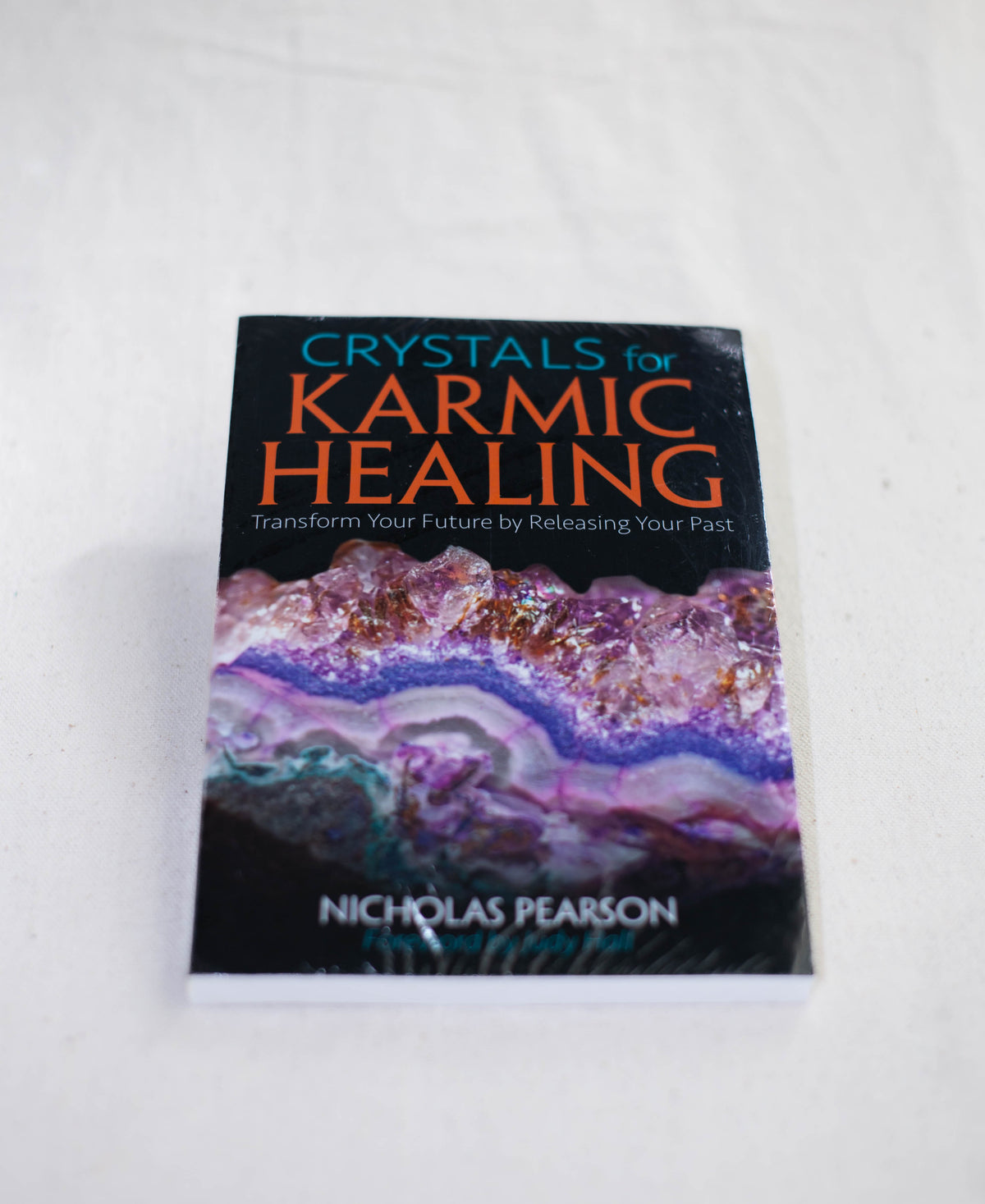 Crystals For Karmic Healing by The Healing Hedge Witch, featuring a vibrant crystal cover, rests on a light surface.