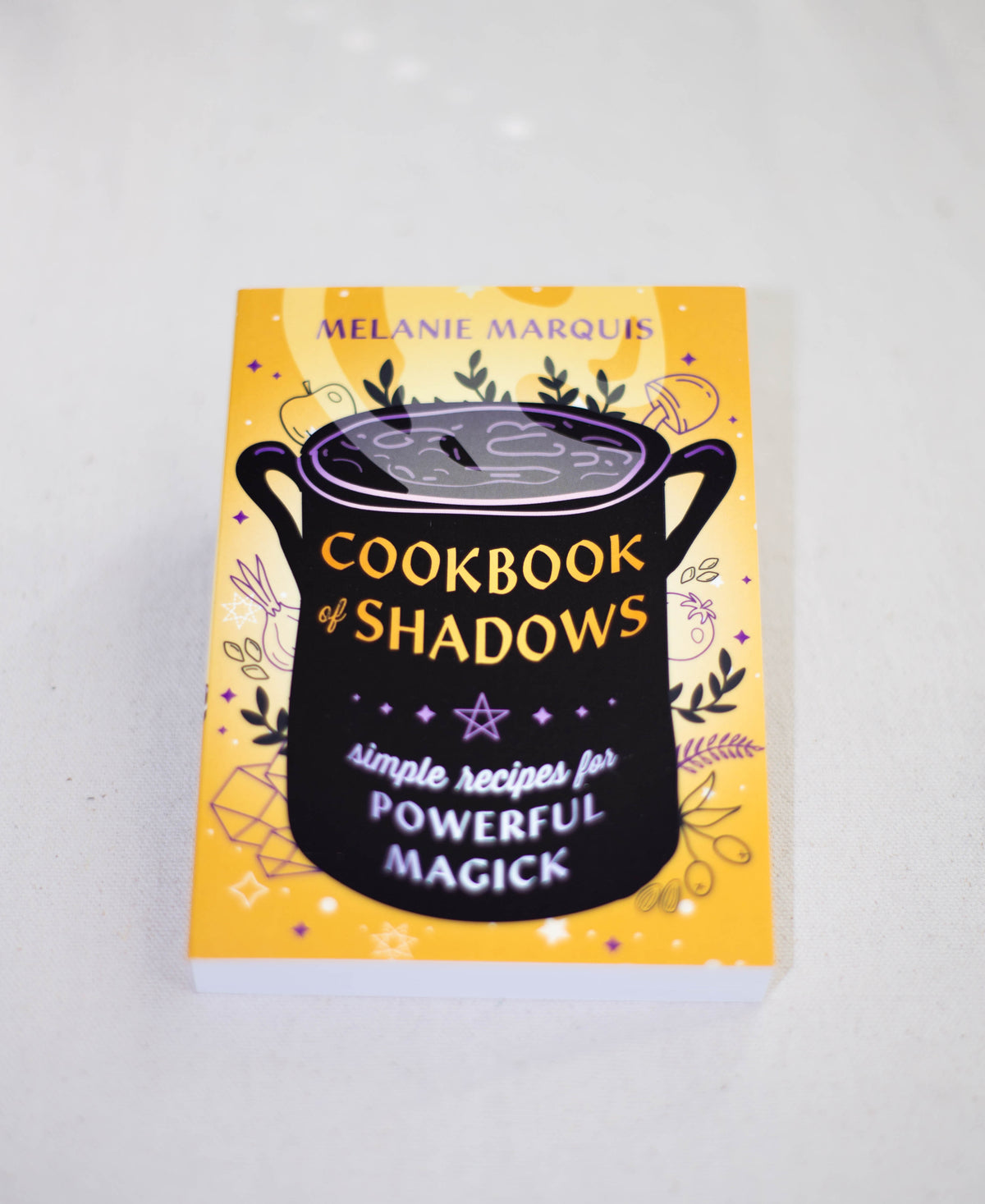 Cookbook of Shadows by The Healing Hedge Witch is a yellow magickal cookbook featuring a black cauldron, potion, mystical symbols, and stars—ideal for simple recipes to achieve your magickal goals.