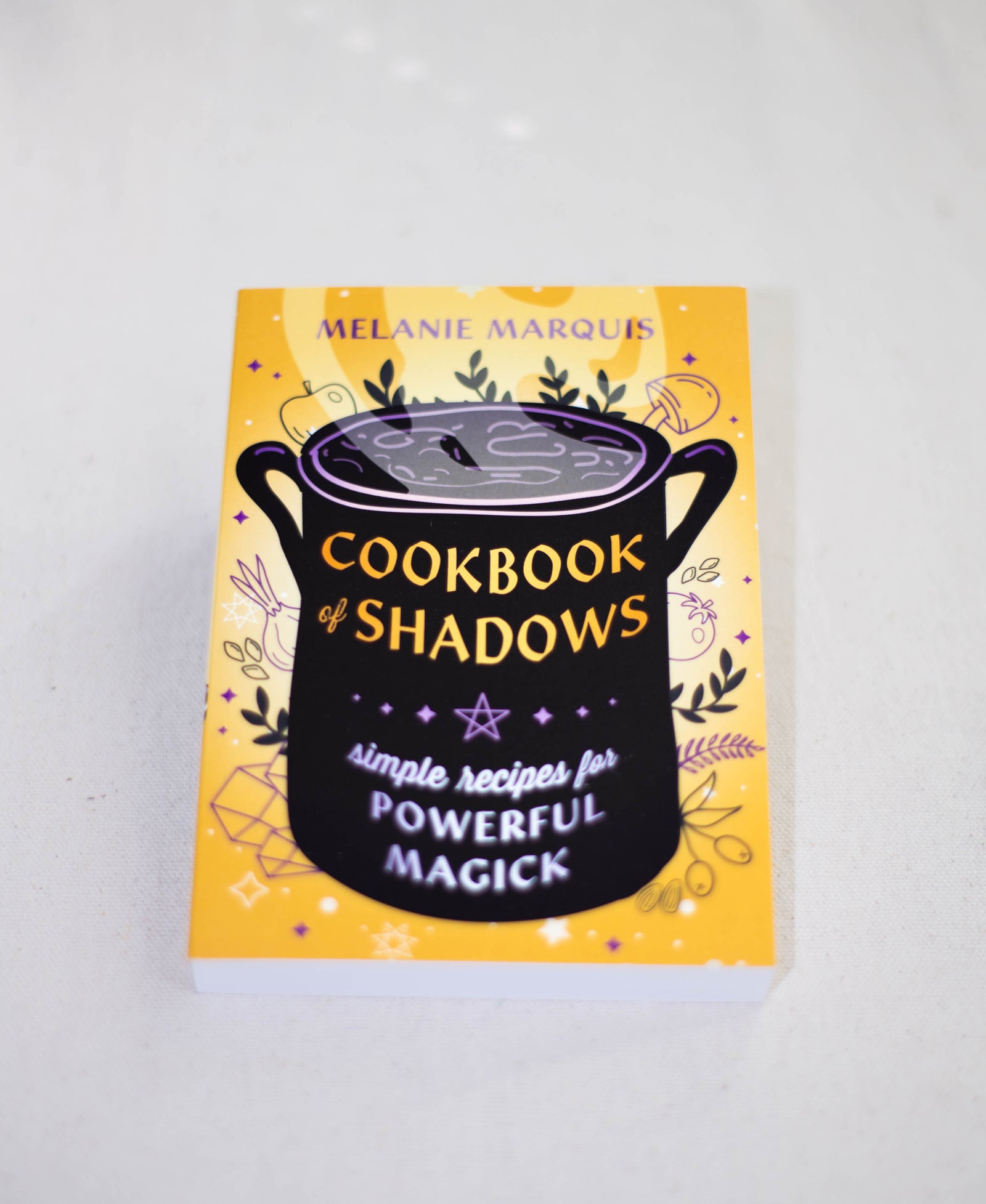 Cookbook of Shadows by The Healing Hedge Witch is a yellow magickal cookbook featuring a black cauldron, potion, mystical symbols, and stars—ideal for simple recipes to achieve your magickal goals.