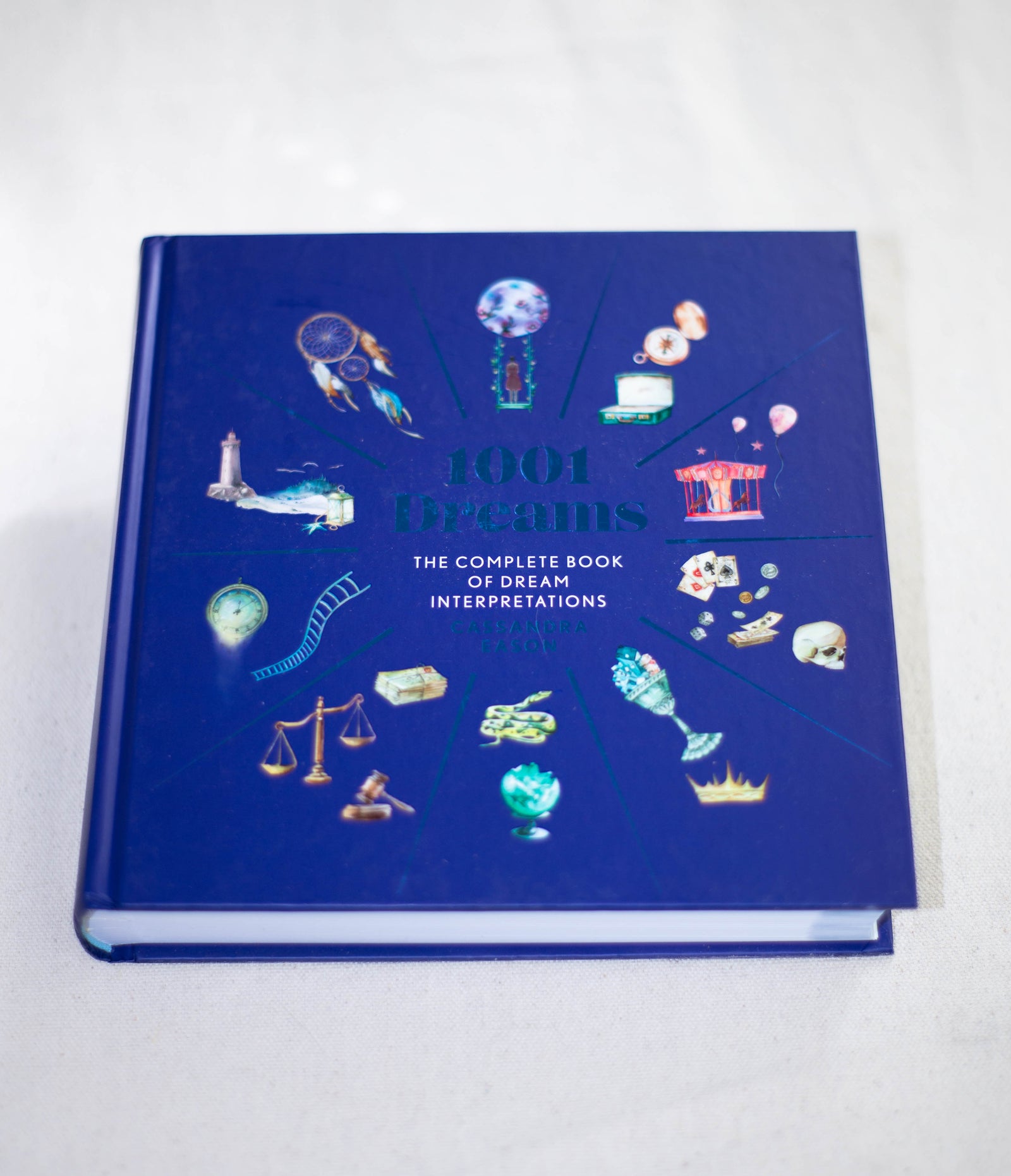 1001 Dreams by The Healing Hedge Witch has a blue cover with small, colorful dream-themed illustrations like a dreamcatcher, crown, key, and scales. It’s the complete book of dream interpretations.