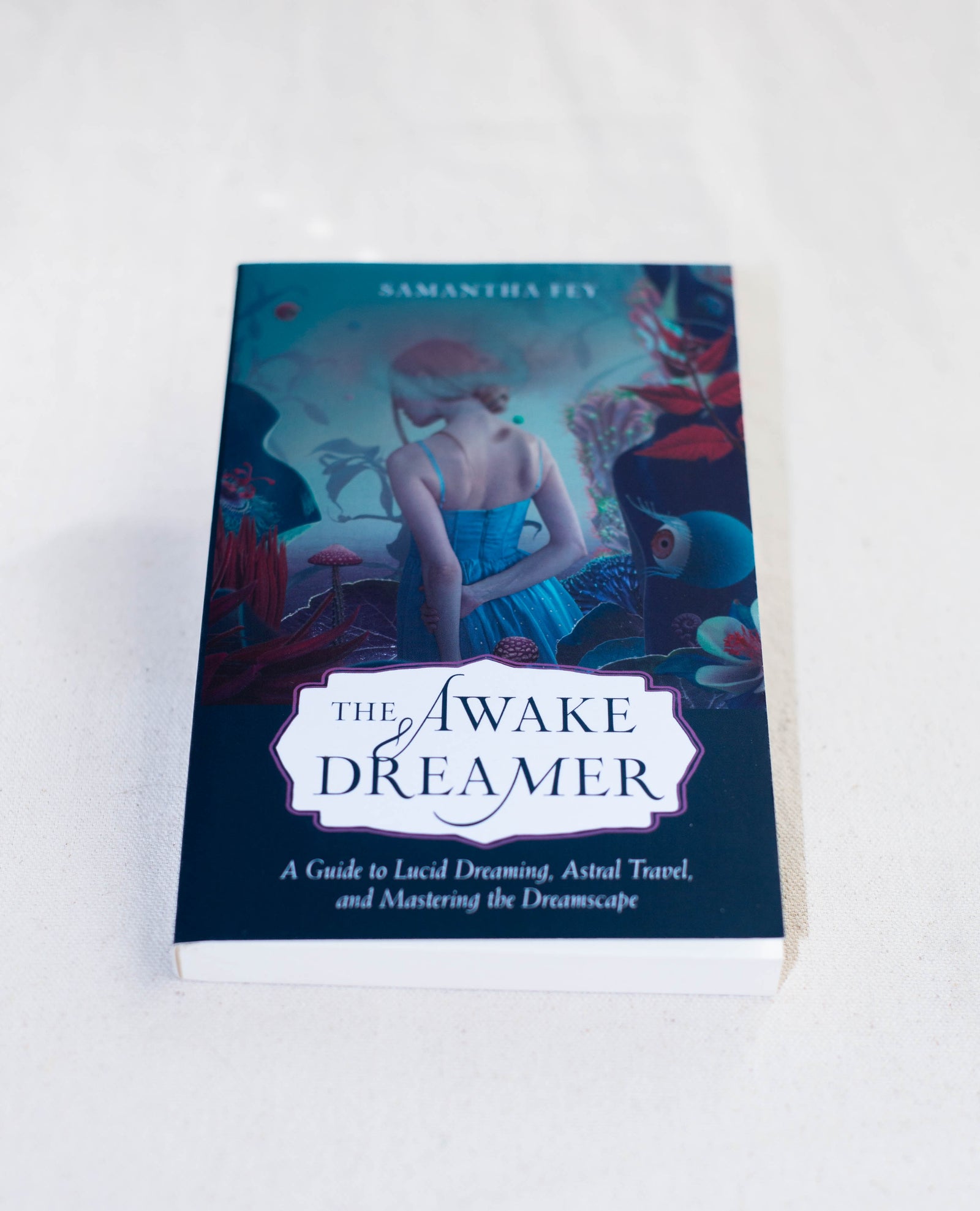 The Awake Dreamer by The Healing Hedge Witch rests on a light surface, its cover showing a short-haired woman in a vibrant, surreal landscape with large plants.