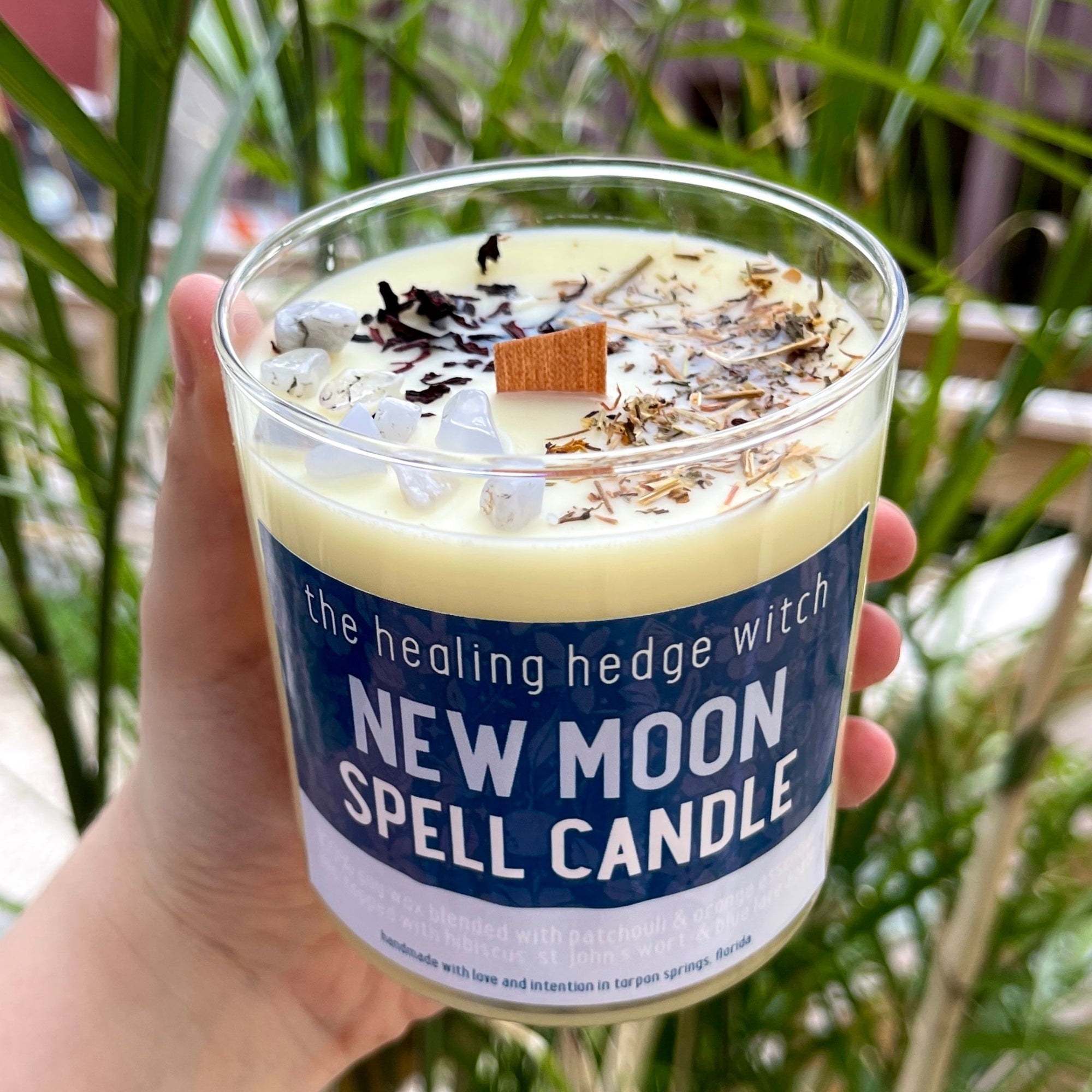 New Moon Spell Candle A hand-poured, small-batch satin soy 8-ounce spell candle made to work with and aid in your manifestation during the new moon. Scented with orange and patchouli essential oils & topped with hibiscus, St. John's Wort, and blue lace agate.