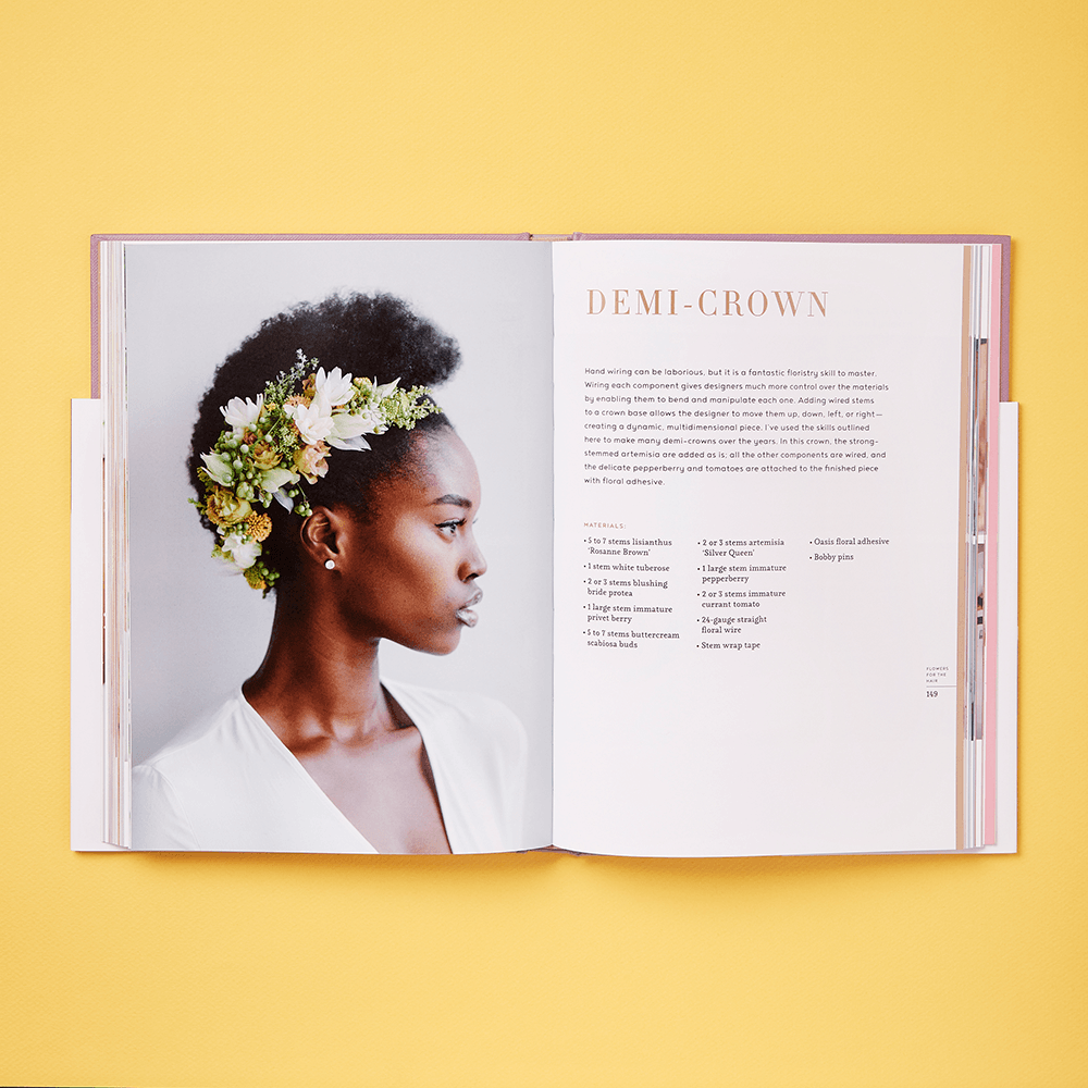 An open copy of "The Art of Wearable Flowers" rests on a yellow surface, displaying a woman in a floral crown on the left page and a “Demi-Crown” tutorial for creating wearable floral accessories on the right.